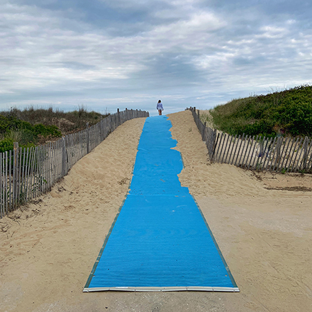 Blue mat stretching over the sand dune to the ocean.